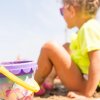 Bambina gioca sulla sabbia vicino a un secchiello colorato.