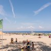 Spiaggia affollata con bandiere, mare e cielo sereno.