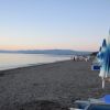 Spiaggia deserta al tramonto, ombrelloni chiusi e mare calmo all'orizzonte.