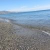 Una spiaggia con ciottoli vicino al mare calmo. Cielo sereno e montagne in lontananza.