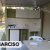 Cucina esterna semplice con tavolo e sedie sotto una tettoia.