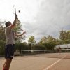 Due persone giocano a tennis su un campo all'aperto circondato da alberi.