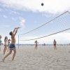 Persone giocano a beach volley su una spiaggia soleggiata.