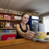 Una barista sorride mentre serve una tazzina di caffè su un banco di legno.