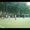 Campo da calcio con persone che giocano, circondato da alberi.