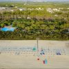 Spiaggia con lettini e ombrelloni, vegetazione e piscina in lontananza.