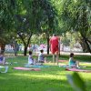 Persone che praticano yoga su tappetini in un parco alberato.