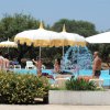 Una piscina con persone, ombrelloni bianchi e gialli e cespugli fioriti sullo sfondo.