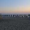 Spiaggia al tramonto con ombrelloni chiusi e rete da pallavolo.