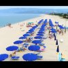 Una spiaggia con file di ombrelloni blu e sedie a sdraio, persone che camminano sulla sabbia.