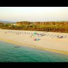 Spiaggia sabbiosa con ombrelloni, mare calmo, vegetazione sullo sfondo.