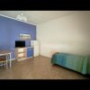 Camera con parete blu, letto singolo con coperta verde, tavolo con sedie, mobile TV e mini frigo.