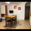 Soggiorno con tavolo e sedie, divano blu, TV a parete e mobile, cucina a lato.