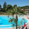 Piscina rotonda con palme, lettini e un'area relax, immersa in un paesaggio verdeggiante.