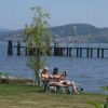 Due persone rilassate su sedie a sdraio vicino a un lago con un molo e colline sullo sfondo.