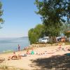 Spiaggia soleggiata con persone che prendono il sole, vista su un lago.