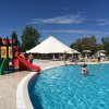 Piscina con scivolo rosso e persone in acqua sotto il sole.