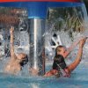 Persone giocano sotto una cascata in piscina.