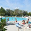 Piscina affollata, persone e lettini sotto ombrelloni.