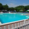 Piscina circondata da sdraio blu e recinzione bianca, con alberi sullo sfondo.