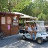 Un golf cart con quattro persone sedute davanti a un chiosco di noleggio bici in un'area verde.