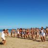 Un gruppo di persone fa esercizi in spiaggia, guidato da istruttori in tenuta bianca.