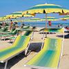 Una spiaggia con lettini verdi e gialli, sotto ombrelloni dello stesso colore, vicino al mare.