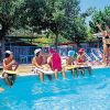 Bambini seduti al bordo di una piscina ascoltano un istruttore.