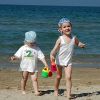 Due bambini piccoli con cappellini giocano sulla spiaggia vicino al mare.
