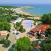 Vista aerea di un villaggio turistico con piscina, alberi e spiaggia sullo sfondo.