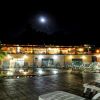 Piscina illuminata di notte con sedie a sdraio e edificio sullo sfondo sotto la luna.