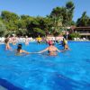 Persone giocano in una piscina all'aperto, circondate da alberi verdi e un cielo limpido.