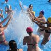 Persone con cuffie colorate giocano in una piscina, spruzzando acqua.