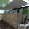 Una casa mobile con tettoia, circondata da alberi e un muretto di pietra.