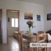 Soggiorno di un bilocale con tavolo da pranzo, sedie e divano. Fotografie appese al muro.