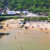 Piccola spiaggia con bagnanti e ombrelloni, circondata da alberi e edifici.