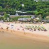 Spiaggia affollata con ombrelloni colorati, mare, e vegetazione verde dietro.
