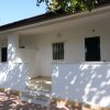Una veranda bianca ombreggiata da alberi con finestre nere e pavimento in pietra.
