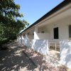 Veranda bianca con tavolino vista su viale pavimentato, affiancato da siepi.