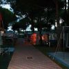 Sentiero in un campeggio, circondato da tende illuminate da luci rossastre al crepuscolo.