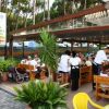 Ristorante all'aperto con tavoli di legno, persone sedute e personale in servizio.