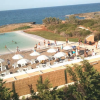 Spiaggia con ombrelloni bianchi e bagnanti, mare sullo sfondo.