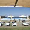 Lettini e ombrelloni bianchi su una spiaggia sabbiosa con una piscina e il mare sullo sfondo.