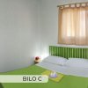 Camera da letto con letto matrimoniale e copriletto verde, finestra con tenda beige.
