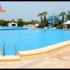 Grande piscina all'aperto con scivolo blu, circondata da palme.