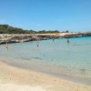 Spiaggia di sabbia con mare cristallino e rocce sullo sfondo.