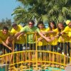 Un gruppo di persone in maglie gialle posa su un ponte giallo, con palme sullo sfondo.