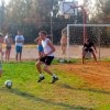 Due ragazzi giocano a calcio su un campo erboso, con una porta e spettatori dietro.