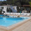 Piscina vuota con lettini bianchi e vegetazione circostante.