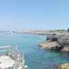 Una vista costiera con mare calmo, scogliera rocciosa e una barca bianca al largo.